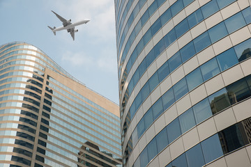 Fototapeta premium Shot of airplane flying above skyscrapers in City of Bangkok dow