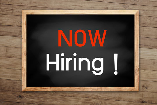 Now hiring concept on chalkboard and background with Brown wood
