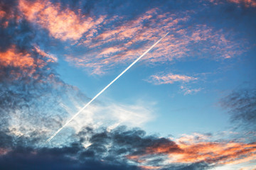Airplane flies in sunset dramatic clouds and leaving trail