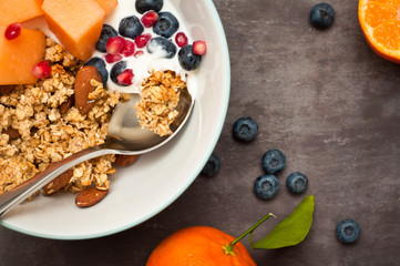 Healthy home made breakfast of crunchy granola muesli, almonds, fresh melon, blueberries and pomegranate seeds. Served with fresh, sliced oranges.