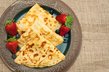 Fresh home made pancakes served on a rustic plate with strawberries and blueberries.