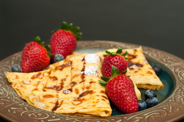 Fresh home made pancakes served on a rustic plate with strawberries and blueberries.