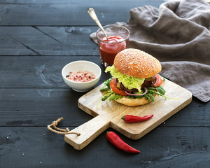 Fresh homemade burger on dark serving board with spicy tomato sauce, sea salt and herbs over black wooden background. Top view.  © sonyakamoz