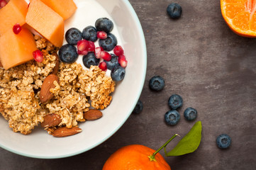 Healthy home made breakfast of crunchy granola muesli, almonds, fresh melon, blueberries and pomegranate seeds. Served with fresh, sliced oranges.