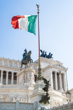View of Italian national flag in front of Altare della Patria (Altar of the Fatherland) , the equestrian sculpture of Victor Emmanuel and statue of the goddess Victoria riding on quadrigas on top