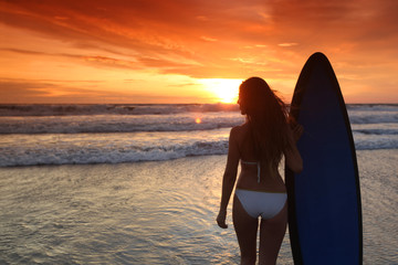 Fototapeta na wymiar Surfer girl on beach at sunset