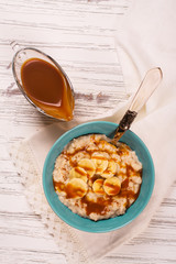 Oatmeal porridge with banana slices, cinnamon and caramel sauce over white wooden table. Selective focus