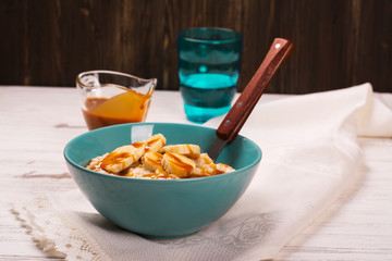 Oatmeal porridge with banana slices, cinnamon and caramel sauce over white wooden table. Selective focus
