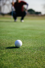 Golf ball with unfocused golfer crouched in the background