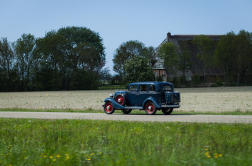 Beautiful blue oldtimer driving on little road near Leeuwarden, Netherlands