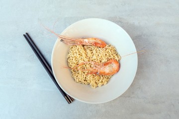 Asian ramen noodles with shrimp in bowl on tile surface and chopsticks - horizontal view from above
