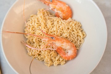 Asian ramen noodles with shrimp in bowl on tile surface and chopsticks - horizontal view from above
