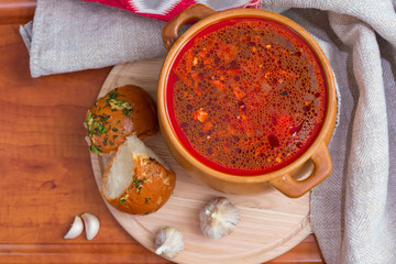 Bursch - Red soup in a clay pot with garlic, bread rolls , carrots , potatoes, onions , beets on a wooden table
