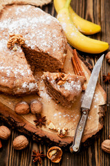 
pastries, cake with walnuts and a banana with powdered sugar on a wooden background