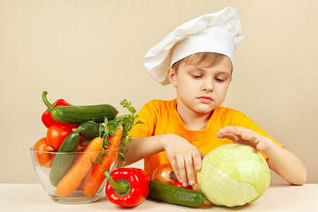 Little funny boy chooses vegetables for salad at the table