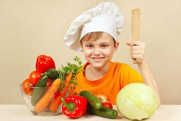 Little boy in chefs hat with fresh vegetables at the table