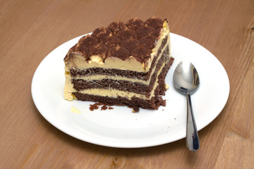 A piece of sponge cake on a white plate with a teaspoon on the wooden table surface. Horizontal photo closeup