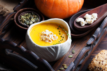 Pumpkin soup with salty popcorn in a white ceramic bowl with fresh pumpkin on a wooden background 