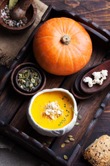Pumpkin soup with salty popcorn in a white ceramic bowl with fresh pumpkin on a wooden background Top view