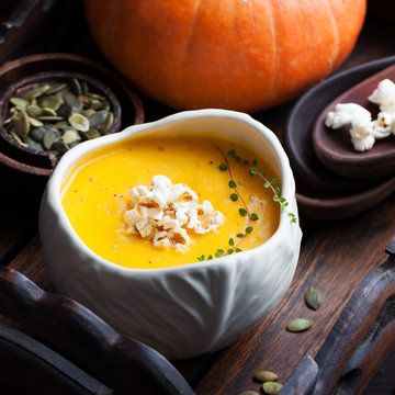 Pumpkin soup with salty popcorn in a white ceramic bowl with fresh pumpkin on a wooden background 
