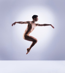 Athletic ballet dancer in a perfect shape performing over the grey background.