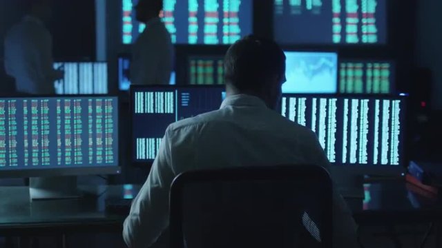 Stockbroker spotted a positive trend in trading charts while working in a dark monitoring room with display screens. Shot on RED Cinema Camera.