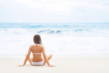 Fototapeta na wymiar Young, beautiful girl sitting on the beach and enjoying the scene of wavy ocean.