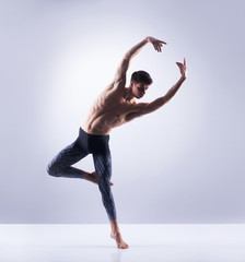 Athletic ballet dancer in a perfect shape performing over the grey background.