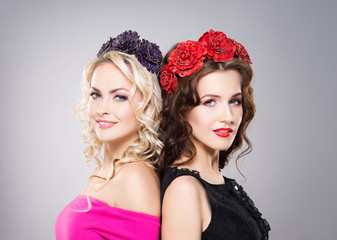 Naklejka premium Portrait of two gorgeous, smiling women wearing flower alike bijouterie over grey background.