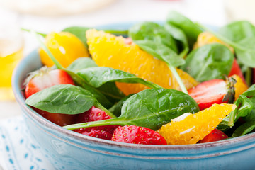Fresh salad with strawberry, orange and spinach in a bowl on wooden background. Copy space