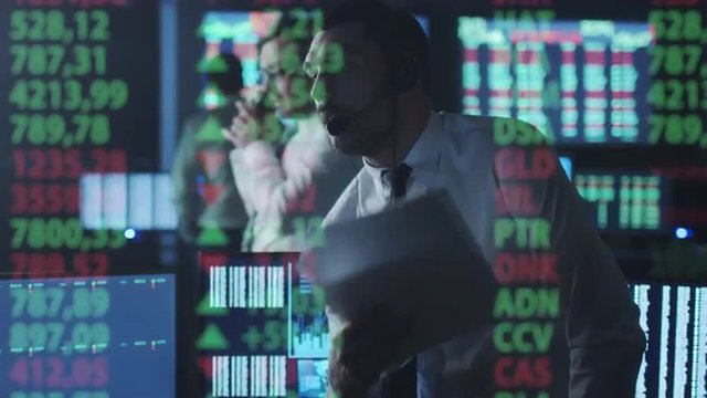 Stockbroker In White Shirt Is Talking On The Phone While Working In A Dark Monitoring Room With Display Screens. Shot On RED Cinema Camera.