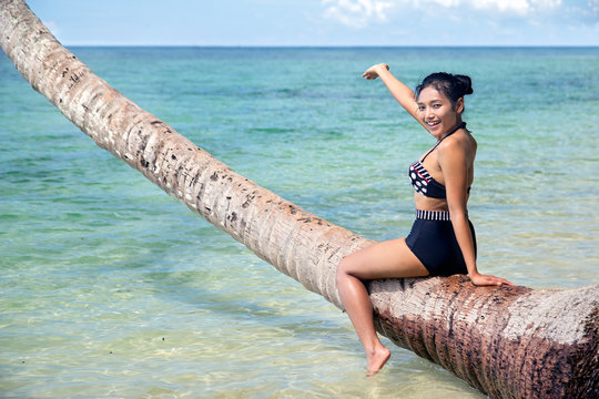 cheerful woman in retro swimsuit sitting on coconut palms and pointing to the sea