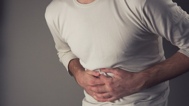Man suffering from stomach ache, severe abdominal pain, holding his belly and having painful cramps.