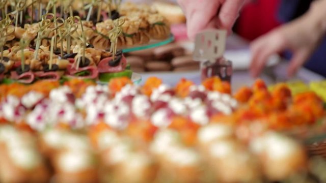 Close up of many canapes set  and snacks on  table and hands picking them. Buffet dinner or stand up party. Handheld shot, rack focus.