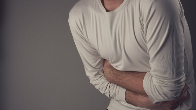 Man suffering from stomach ache, severe abdominal pain, holding his belly and having painful cramps.