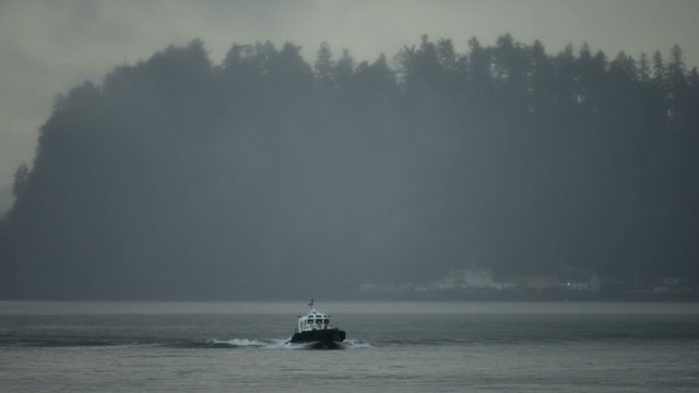 A Pilot boat on the Columbia river in Astoria, Oregon in a wide shot. Fog obscured buildings and trees on the Washington side of the river in the background.