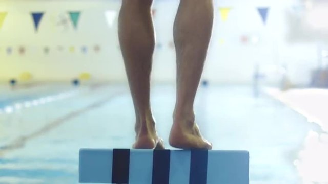Jib Shot from Back Side of Professional Male Swimmer Preparing and Jumping Off the Starting Block into Pool. Shot on RED Cinema Camera.