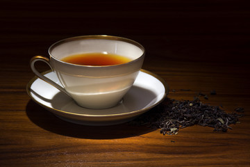 porcelain cup with tea and some loose tea on a wooden table