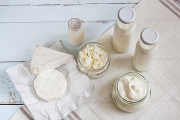 Dairy products. Milk in glass bottle, yogurt, sour milk cheese, sour cream in glass jar, camembert, brie on light blue wooden table