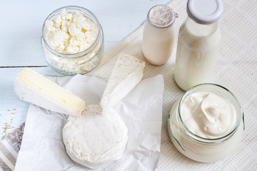 Dairy products. Milk in glass bottle, yogurt, sour milk cheese, sour cream in glass jar, camembert, brie on light blue wooden table