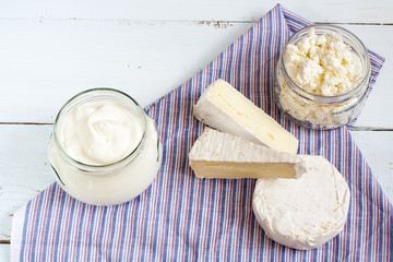 Dairy products. Sour milk cheese, sour cream, camembert and brie with checkered napkin on light blue wooden table