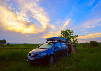 The camping with a tent and  car at sunrise in  field.