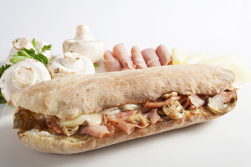 Sandwich with grilled ham, button mushrooms and cheese in a bun placed beside fresh button mushrooms, ham and cheese.