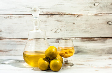 Quince liqueur in a cerafe and glass on wooden background