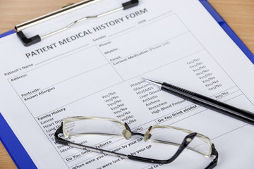 Patient medical history form on clipboard with pen and eyeglasses