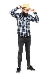 Bearded young hipster adjusting straw hat visor looking away. Full body length portrait isolated over white studio background.