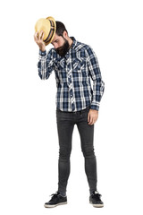 Serious bearded hipster taking off straw hat looking down. Full body length portrait isolated over white studio background.