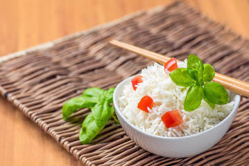 Cooked basmati rice in a bowl with chipsticks, tomato and basil