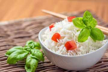 Cooked basmati rice in a bowl with chipsticks, tomato and basil