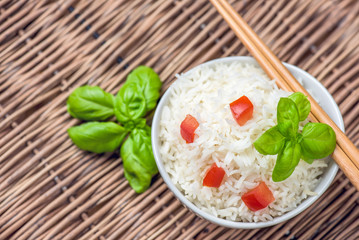 Cooked basmati rice in a bowl with chipsticks, tomato and basil